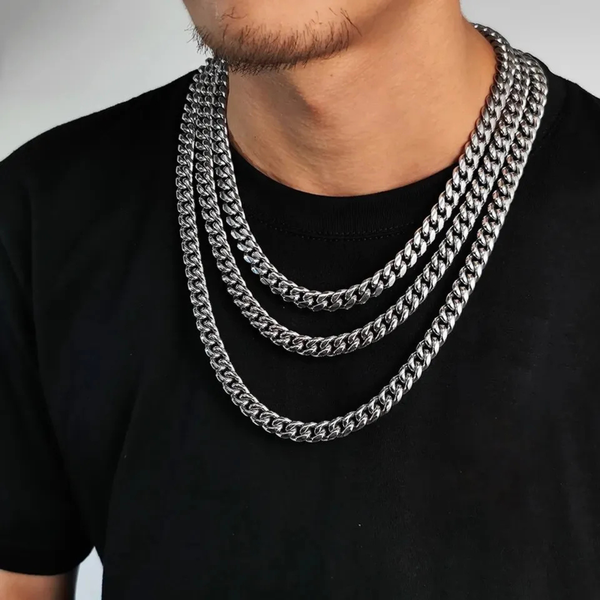 Male model wearing layered silver Cuban chain necklaces against a plain background.