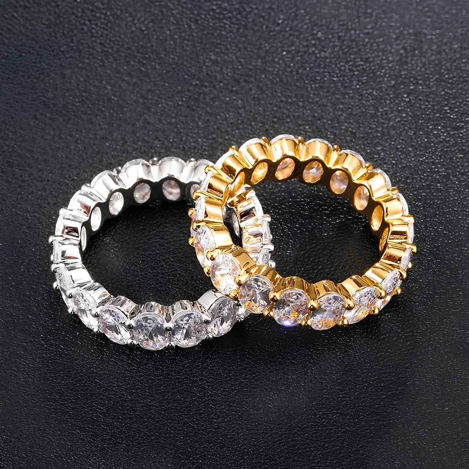 Two oval cut cubic zirconia rings on a textured black background, one in silver and one in gold,.