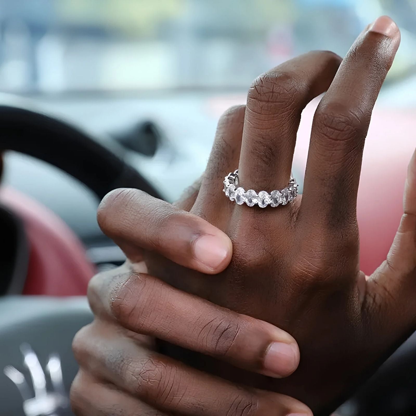 A close-up of a person's hands inside a car, wearing a silver-toned ring with a row of clear, cubic zirconia stones.