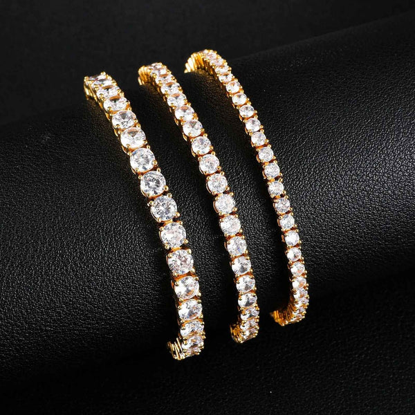 Three gold tennis bracelets with clear cubic zirconia stones on a black background