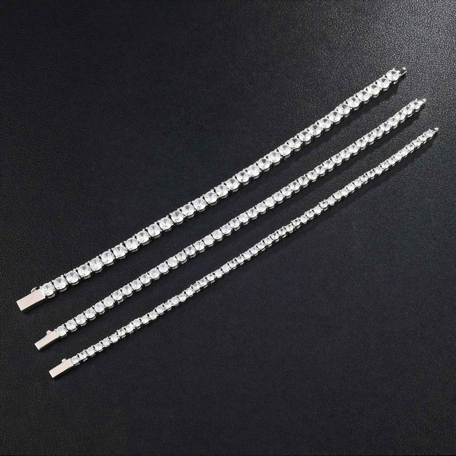 Three silver tennis bracelets with clear cubic zirconia, displayed diagonally on a dark textured background.