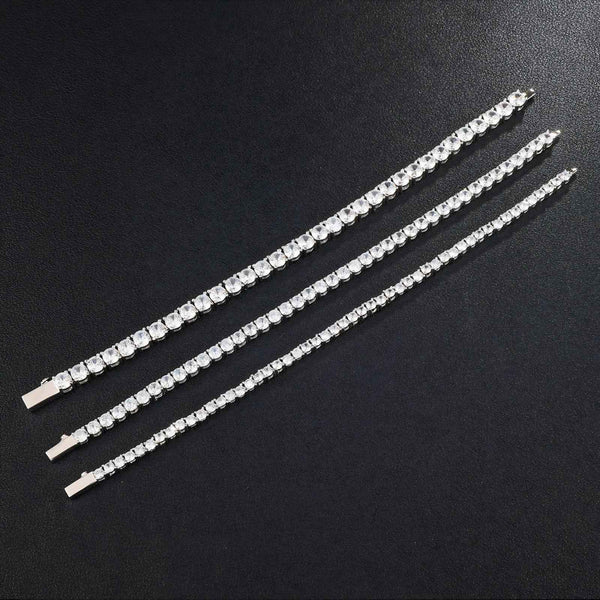 Three silver tennis bracelets with clear cubic zirconia, displayed diagonally on a dark textured background.