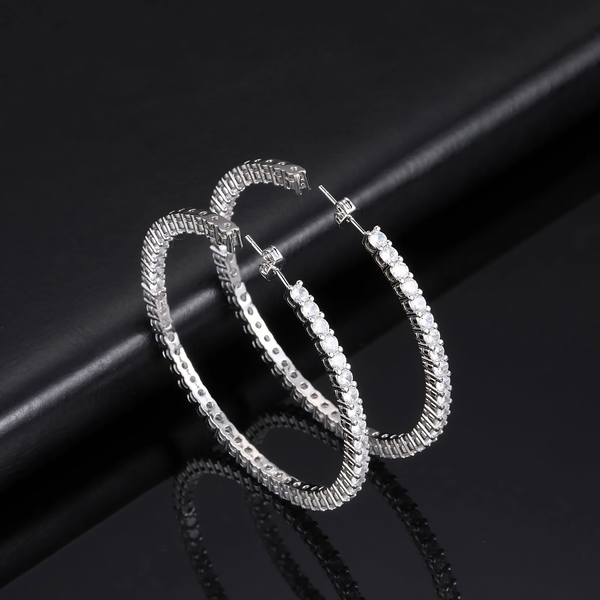Angled view of silver eternity hoop earrings on black background