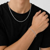 A close-up of a person wearing a silver twisted rope chain necklace and a matching silver bracelet, styled with a black t-shirt against a light gray background.