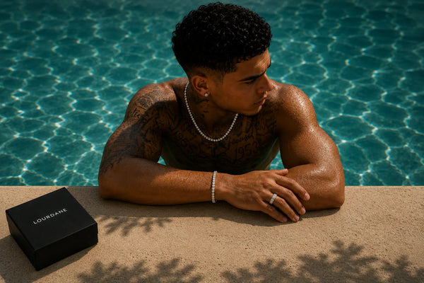 Male model wearing a silver chain, bracelet and ring beside a swimming pool with a Lourdane jewellery box.